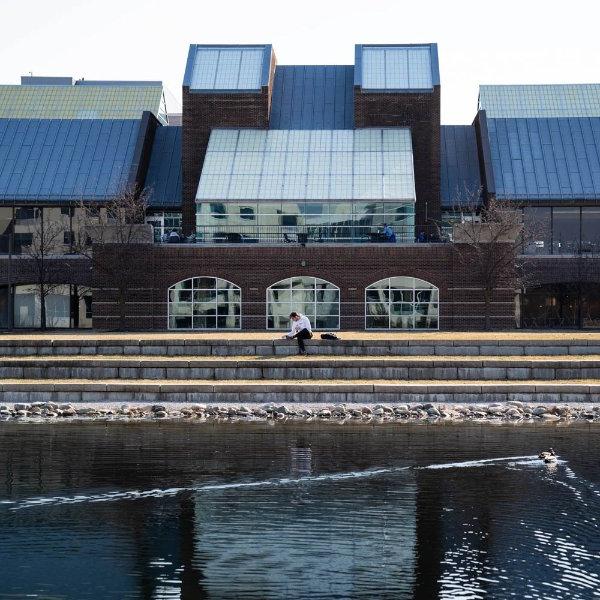 池塘上的一只鸭子和一个坐在分层区域上的人是建筑物的前景.