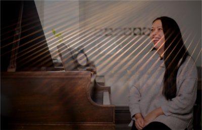 A person sitting at a piano smiles as filtered sunlight beams through.