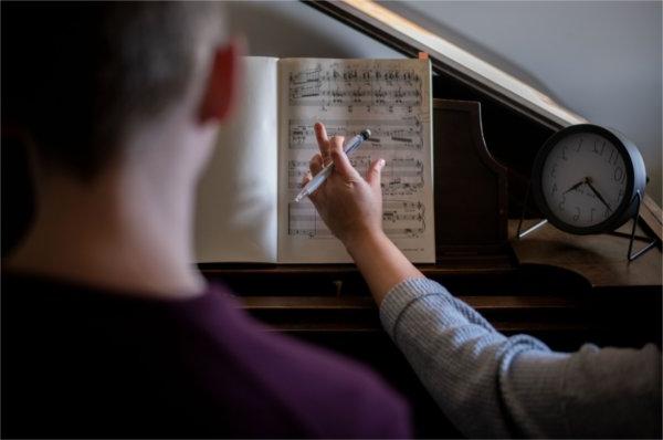 The back of a student is seen 和 the arm of a piano teacher, 手里拿着笔, 指着一本音乐书.