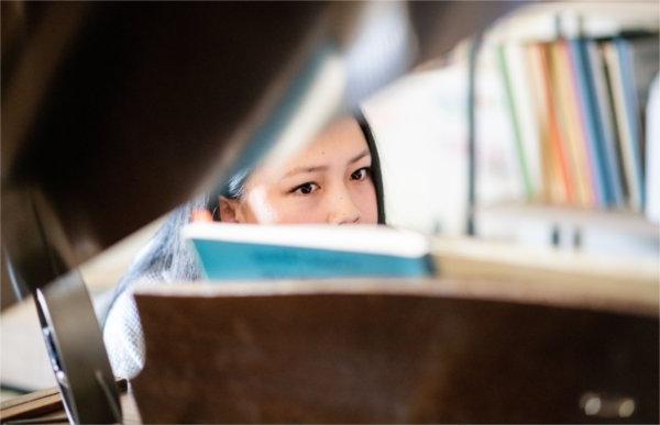 A person seen through the opened top of a baby gr和 piano peers at a music book.