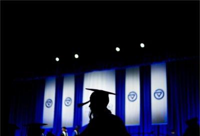 A silhouetted graduate walks in front of the stage during 毕业典礼 ceremonies.