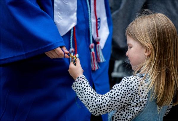 A young girl plays with a graduate's cords.