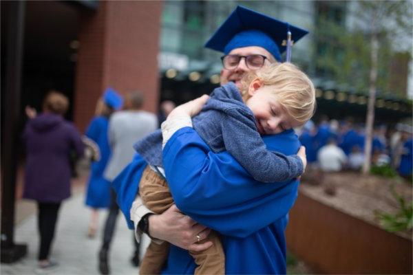A graduate hugs a young child tight following 毕业典礼 ceremonies. 