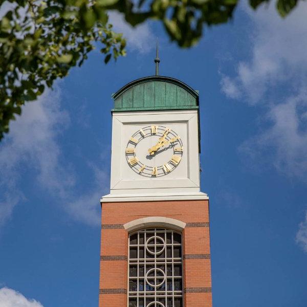 The top of a carillon with a clock is shown with tree branches in the foreground.