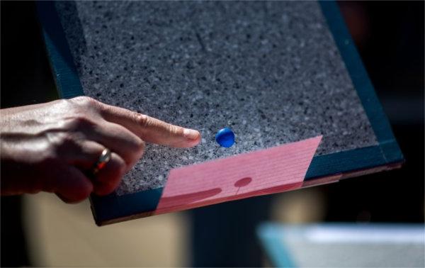 一个人的食指指向一张粉红色卡片旁边的一个蓝色小球.