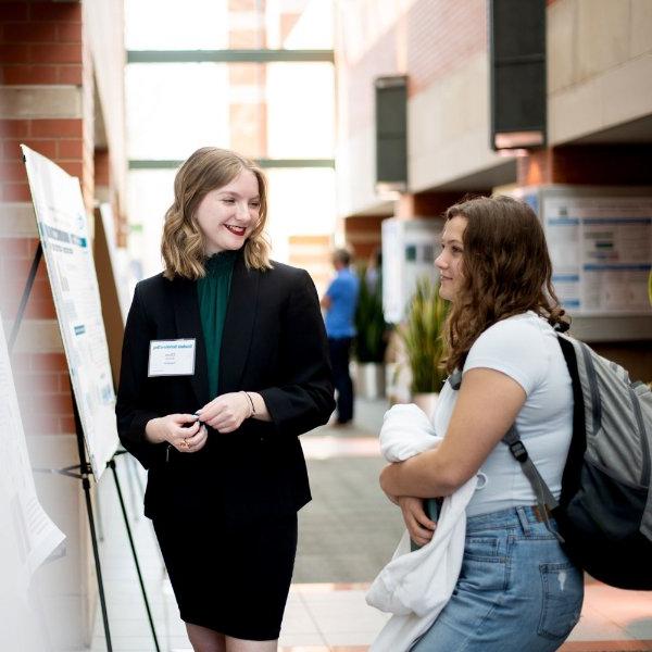 A student discusses her research with another student during Student Scholars Day