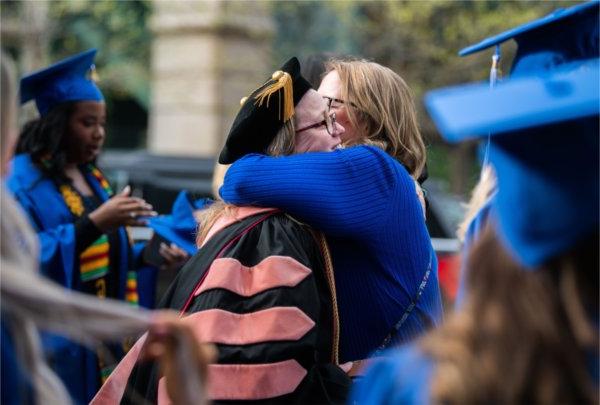  在毕业典礼前，一个人拥抱了一名身着长袍的教员.