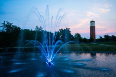 Zumberge Pond fountain lit in blue at twilight with carillon tower in background