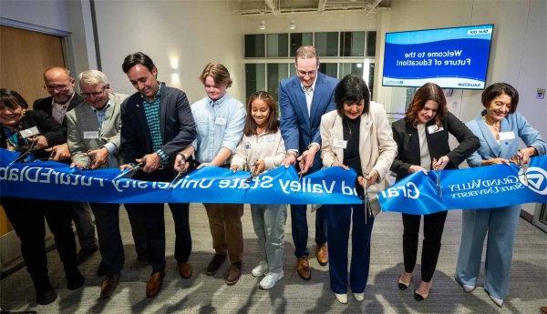 Several people cut into a ribbon with the Grand Valley State University logo 和 words "Grand Valley State University futureEDlab." A screen behind them says, "Welcome to the Future of Education!" "Blue Dot" and "futureEDlab." The GVSU logo is also on the screen.